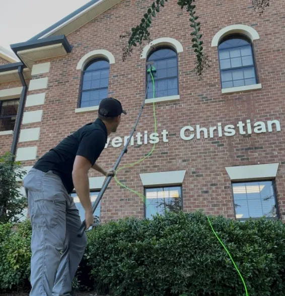 A Diamond Residential technician cleaning second-storey windows on a brick building with a waterfed pole, from the ground.