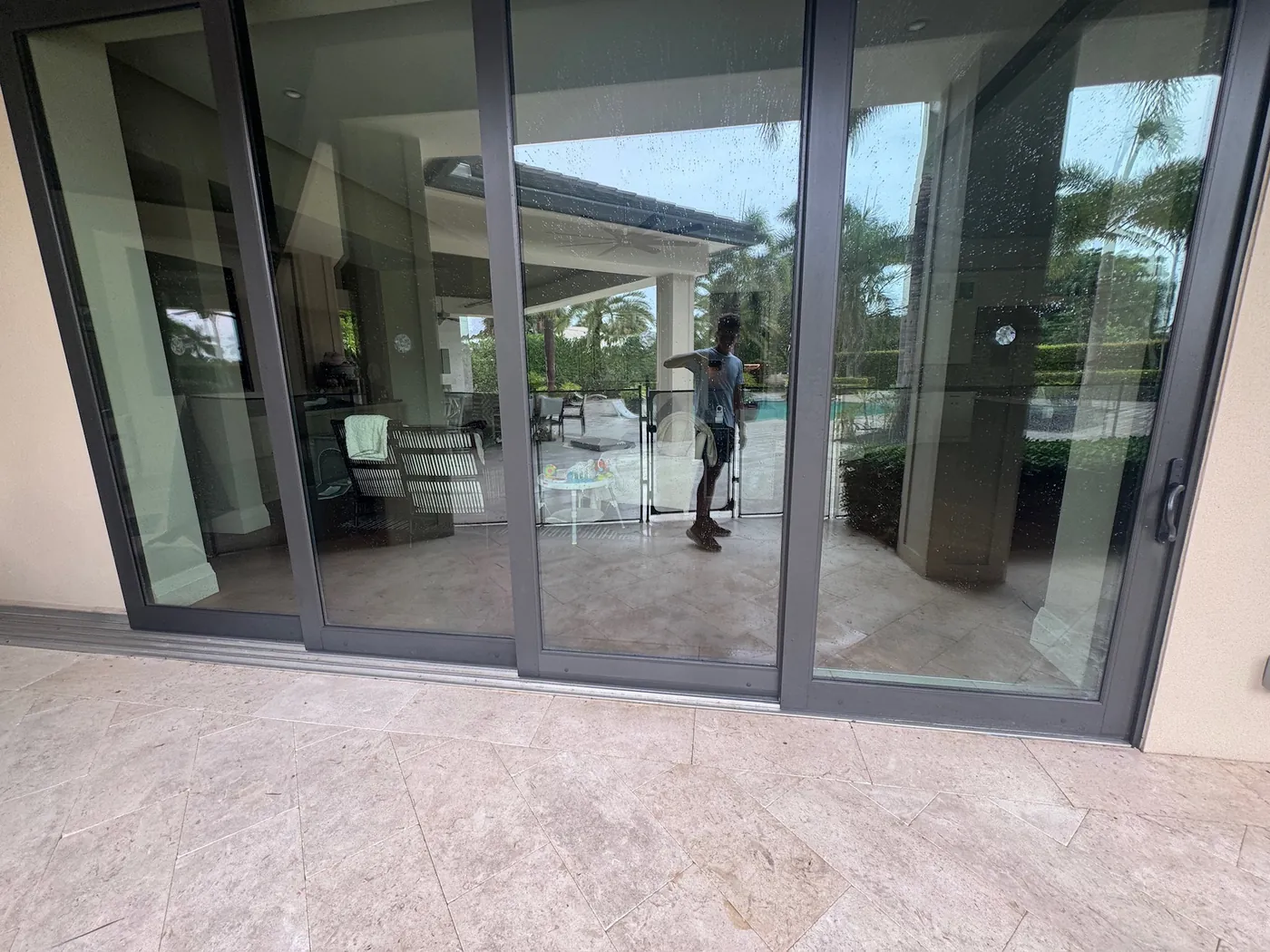 A cleaned wall of sliding glass doors reflecting the technician and the pool deck behind him.