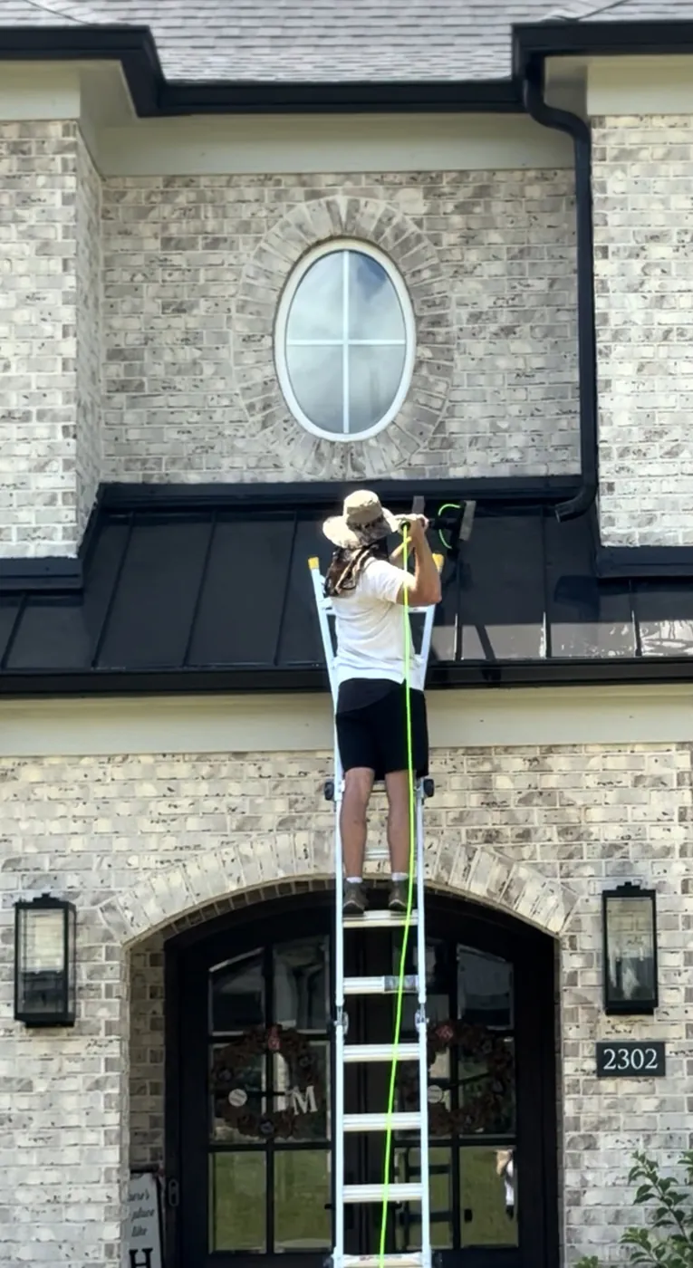 A Diamond Residential technician on a ladder cleaning the arched upper-storey window above the front door of a brick home.