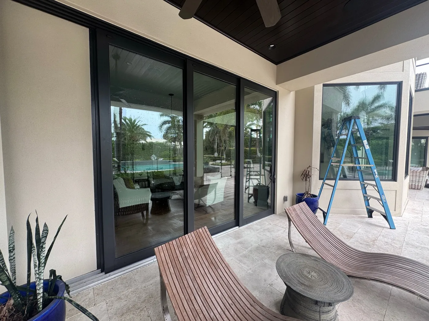 Cleaned sliding glass doors on a covered lanai, with a step ladder set up and a pool beyond.